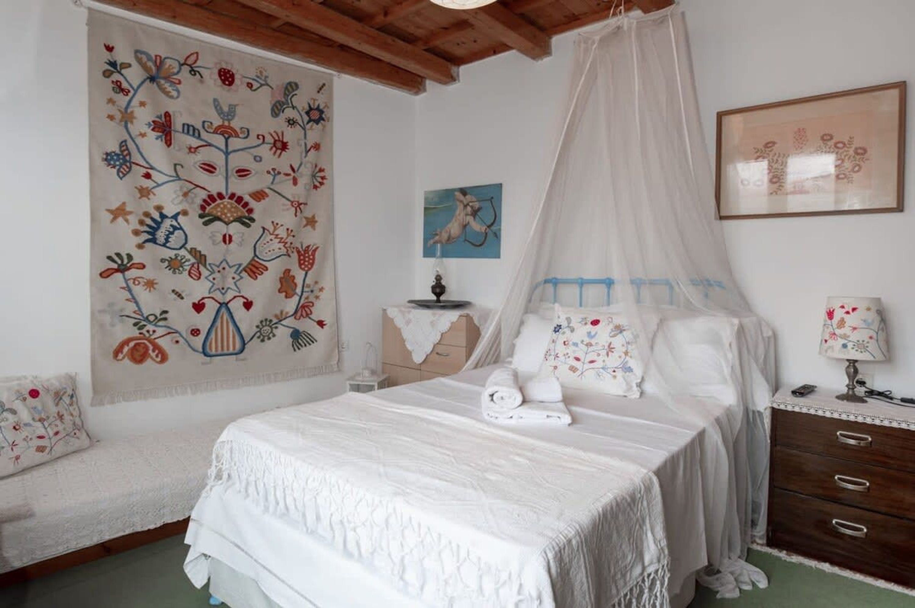 Quarto com cama, mesa de cabeceira, cômoda, tapeçaria e um quadro na parede.