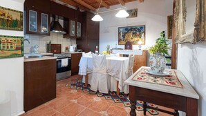 A kitchen with wooden cabinets, a tiled backsplash, a stove, and a dining area with a table set for two. - Cretan Magnolia Gem - Smari Cozy Getaway (Minoa Pediada)