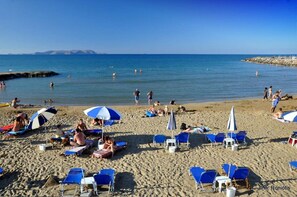 A beach with blue and white umbrellas, sun loungers, and people swimming in the water.