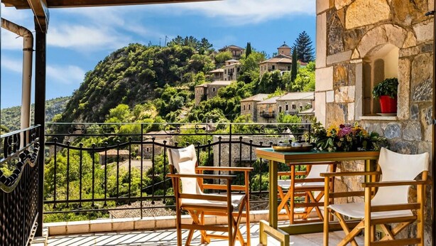 A balcony with a view of a hillside village, stone walls, and a table with chairs.