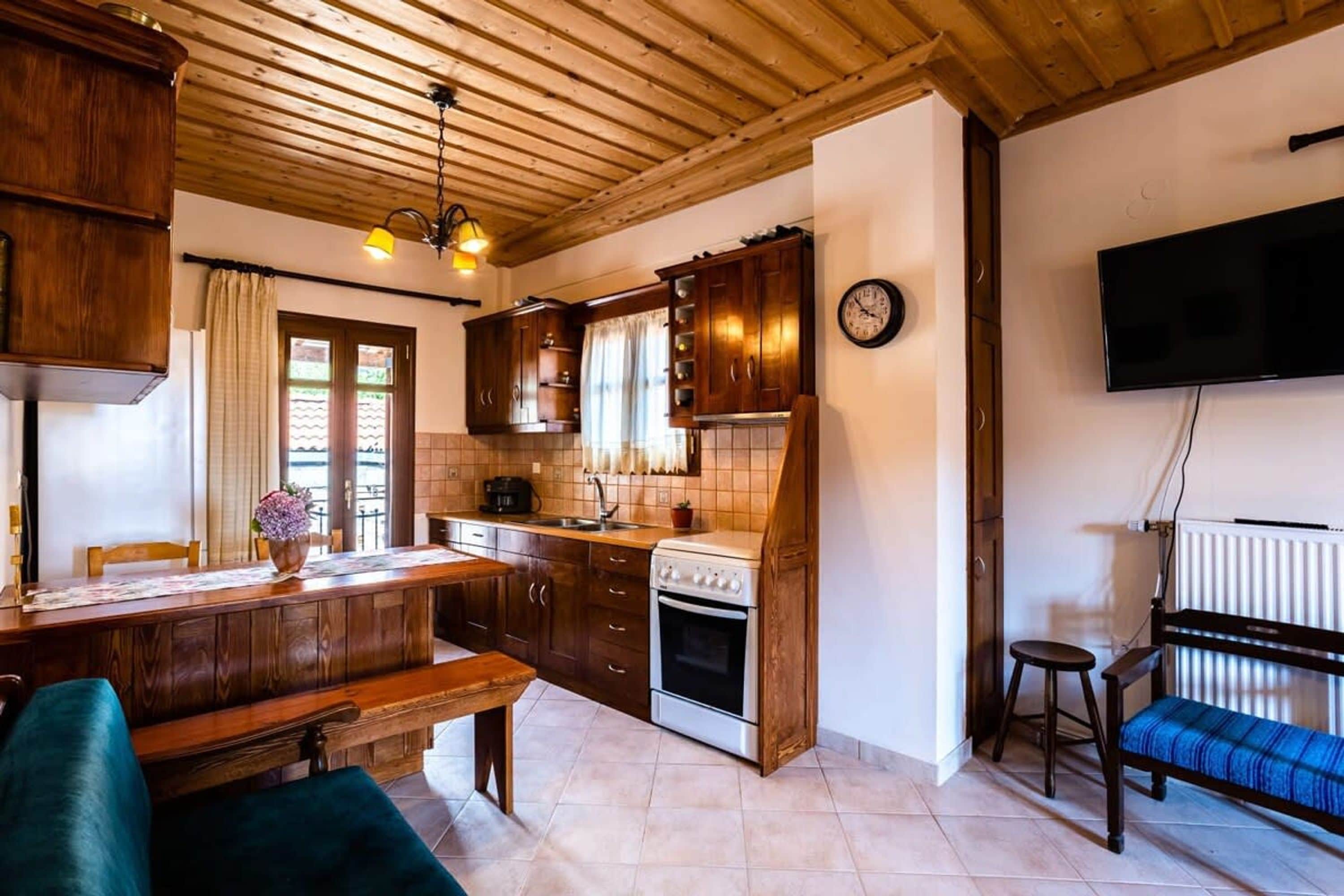 A kitchen with wooden cabinets, a stove, a dining table with chairs, and a bench.