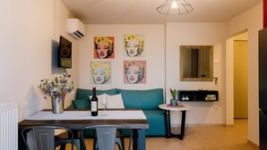 A modern living room with a teal sofa, a dining table with chairs, and wall art. - Urban Living Minicasa Nomad - Kalamata s Hideaway (Kalamata)