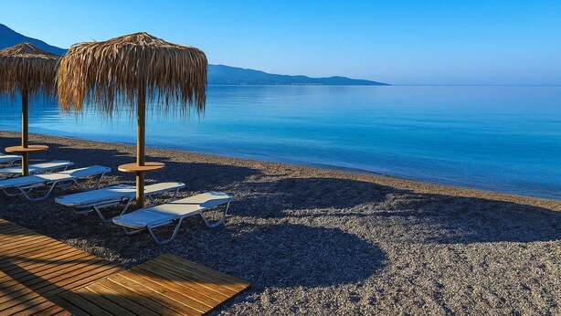 A beach with lounge chairs and straw umbrellas. - Urban Living Minicasa Nomad - Kalamata s Hideaway (Kalamata)