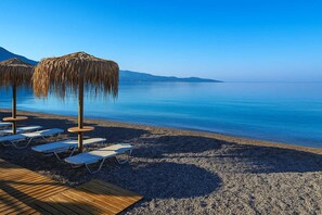 A beach with lounge chairs and straw umbrellas. - Urban Living Minicasa Nomad - Kalamata s Hideaway (Kalamata)