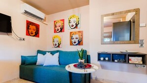 A teal sofa with white cushions, a small round table with a plant, and a mirror above it. - Urban Living Minicasa Nomad - Kalamata s Hideaway (Kalamata)