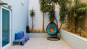 A modern outdoor seating area with a cushioned chair, a bench with colorful cushions, and tall plants. - Urban Living Minicasa Nomad - Kalamata s Hideaway (Kalamata)
