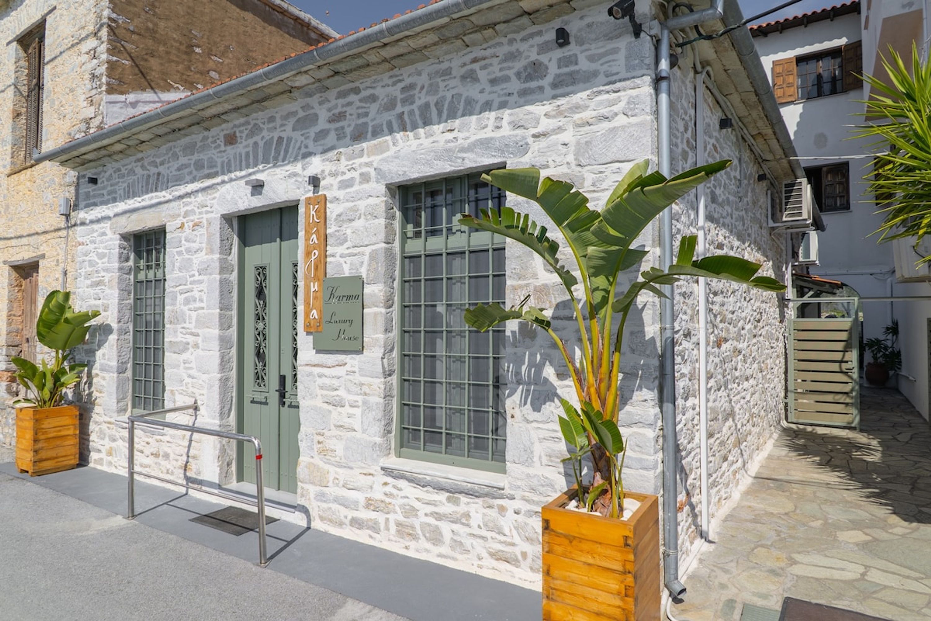 Un bâtiment en pierre avec une porte et des fenêtres vertes, une enseigne indiquant « Maison de luxe » et des plantes en pot.