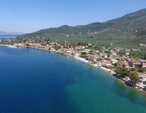 A coastal town with buildings along the waterfront, a clear blue sea, and green hills in the background. - Seafront Karma Luxury - An Escape From Reality (South Pelion)