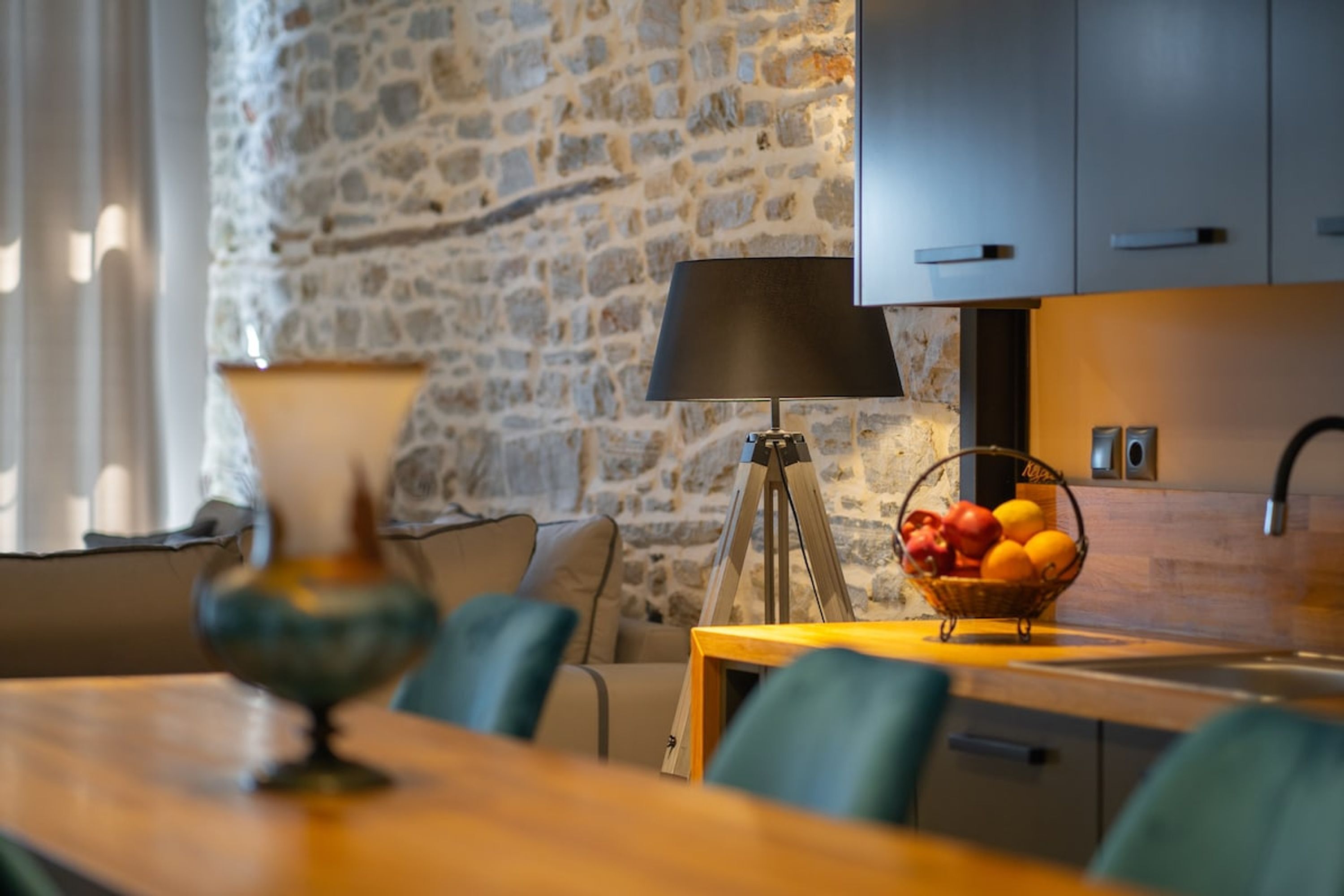 A dining area with a stone wall, a lamp, a fruit basket, and modern cabinetry.