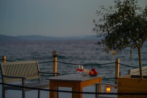 A wooden table with two glasses of red wine, a candle, and a bowl of fruit on a deck overlooking the sea. - Seafront Karma Luxury - An Escape From Reality (South Pelion)