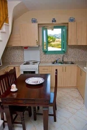 A compact kitchen with a dining table, a stove, and a window with a view of greenery. - Skyros Luxury Poolside Getaway (Skiros)
