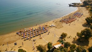 An aerial view of a beach with rows of umbrellas and sun loungers, a clear view of the sea, and a distant cityscape. - Maria s Serene Countryside Retreat by Chania (Chania)