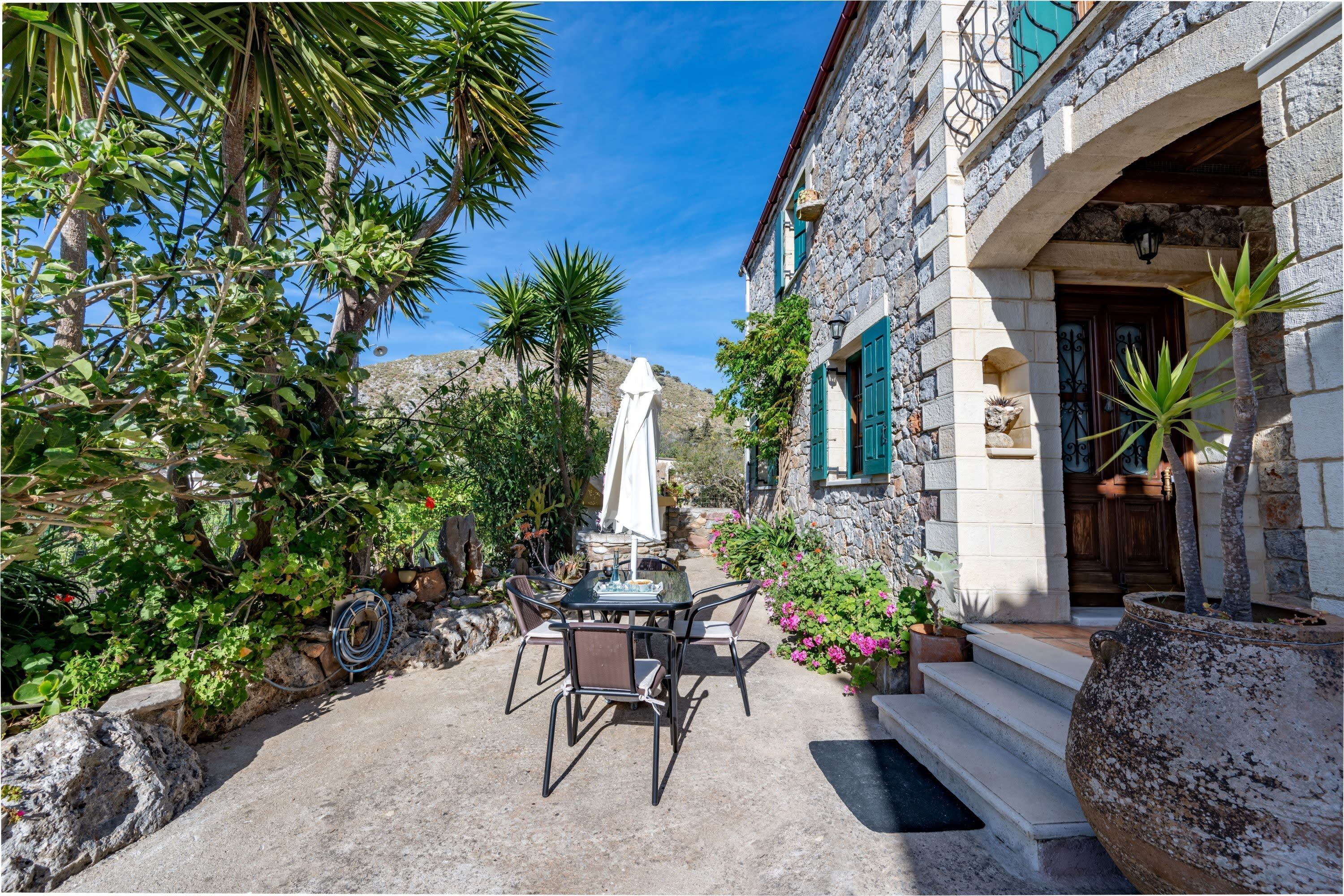 A stone building with a balcony, a table with chairs, and a potted plant.
