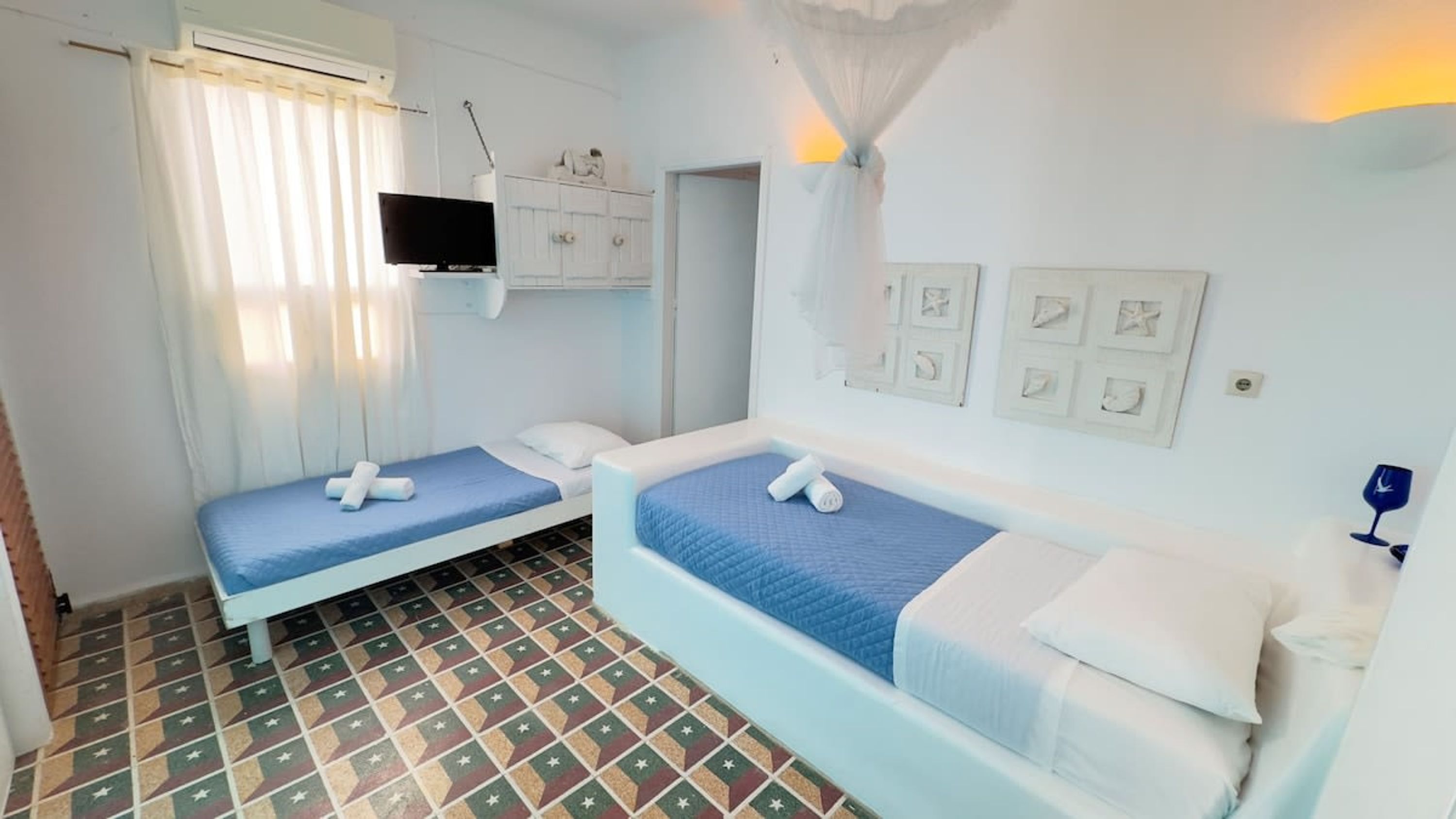 Une petite chambre propre, avec deux lits, une télévision et un sol carrelé.