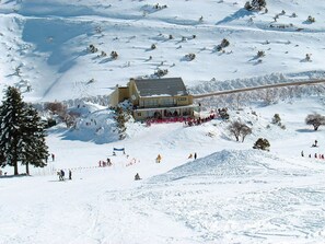 Estació d'esquí amb una cabana, pistes cobertes de neu i un teleàs.