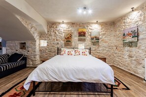 Un dormitori amb paret de pedra, un llit amb estovat blanc, un sofà negre i un terra de fusta.