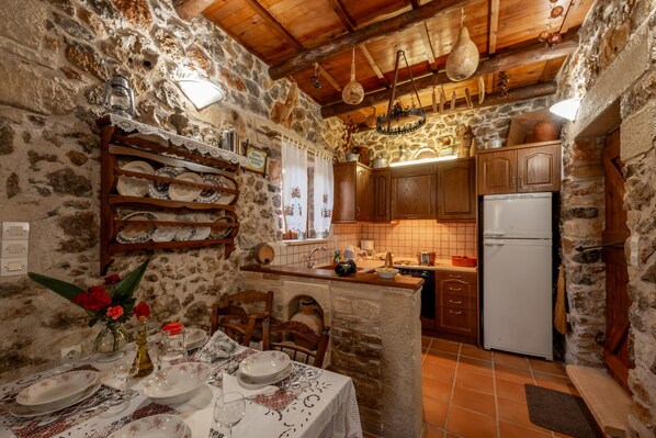 A rustic stone kitchen with wooden cabinets, a white refrigerator, and a dining area with a table set for four.