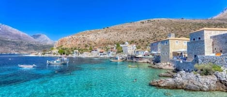 A coastal village with stone buildings, clear turquoise water, and boats.