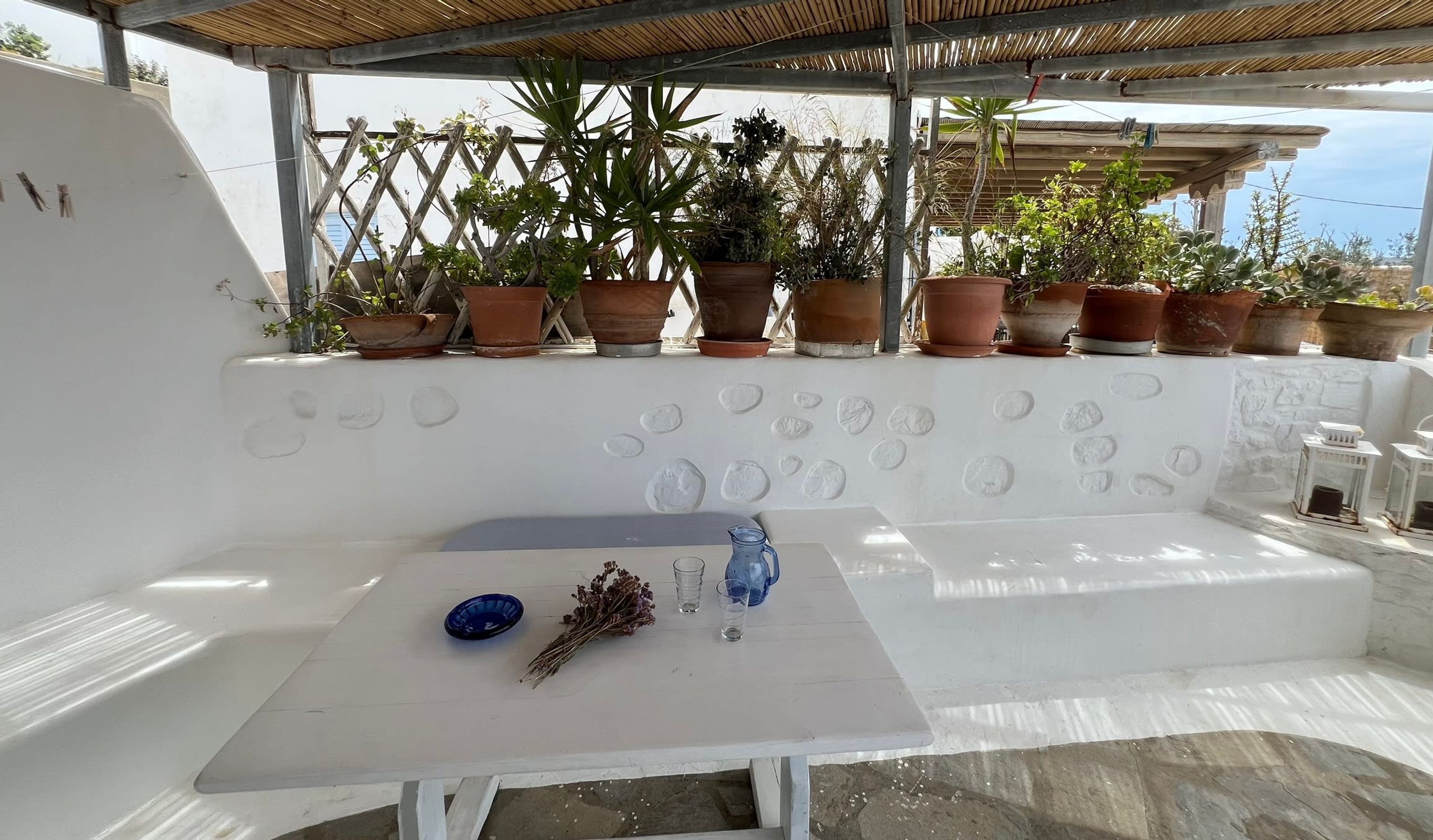 A white outdoor seating area with a table, potted plants, and a decorative wall.