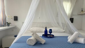 Ein ordentlich bezogenes Bett mit einer blauen Steude, weißen Kissen und einem weißen Baldachin.