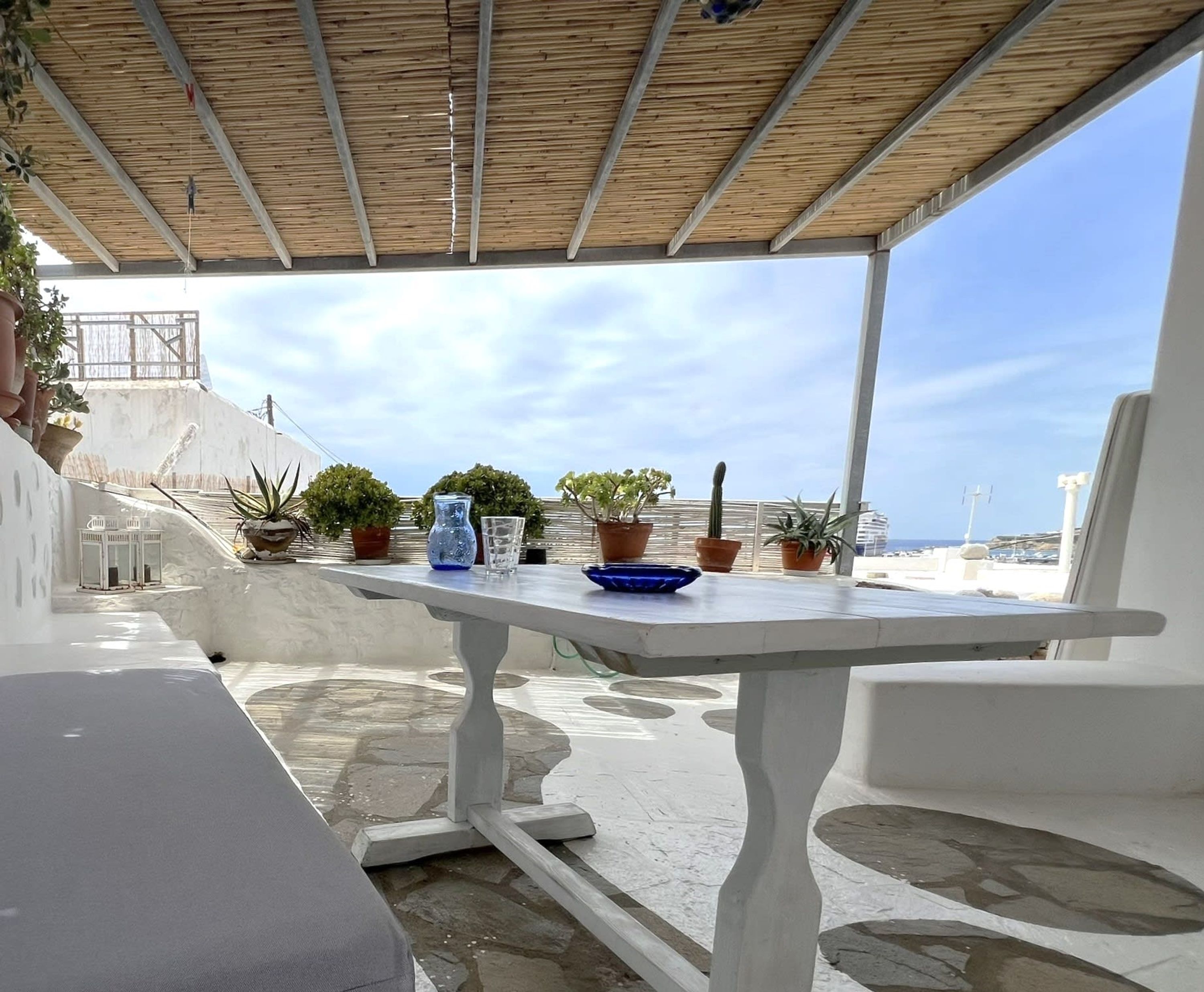 Un espacio al aire libre cubierto con una mesa, plantas en macetas y vistas al mar.