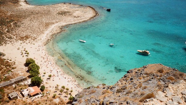 A coastal beach with clear turquoise waters, boats, and a few buildings. - Seaside Oasis Near Heraklion Villa Maro IV Suite (Hersonissos)
