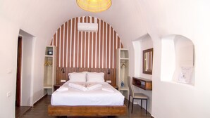 A bedroom with a wooden bed, white walls, striped wallpaper, and a hanging light fixture. - Santorini Rooftop Hot Tub Suite w Panoramic Views (Santorini)