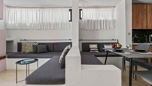 A modern living space with a grey sofa, a small round table, and a kitchen area with a black countertop and wooden cabinets.
