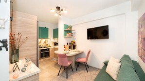 A compact living space with a kitchenette, dining area, and a green sofa. - Urban Bloom Oasis - Mini Zen Maison (Kalamata)