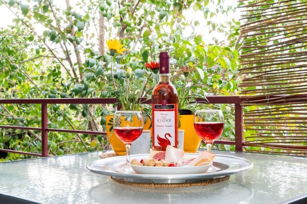 A table with a bottle of red wine, two glasses of red wine, and a plate with cheese and nuts on a glass table.