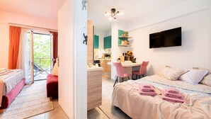 A modern hotel room with a balcony, a kitchenette, a dining area, and a bed with neatly folded towels. - Urban Bloom Oasis - Mini Zen Maison (Kalamata)