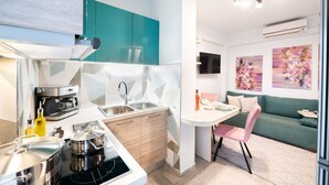 A compact kitchen with teal cabinets, a coffee machine, and a sink. There's a dining area with a table, chairs, and a sofa. - Urban Bloom Oasis - Mini Zen Maison (Kalamata)