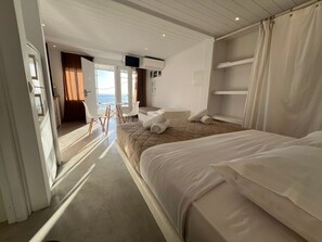 A hotel room with a bed, a desk, and a view of the sea.
