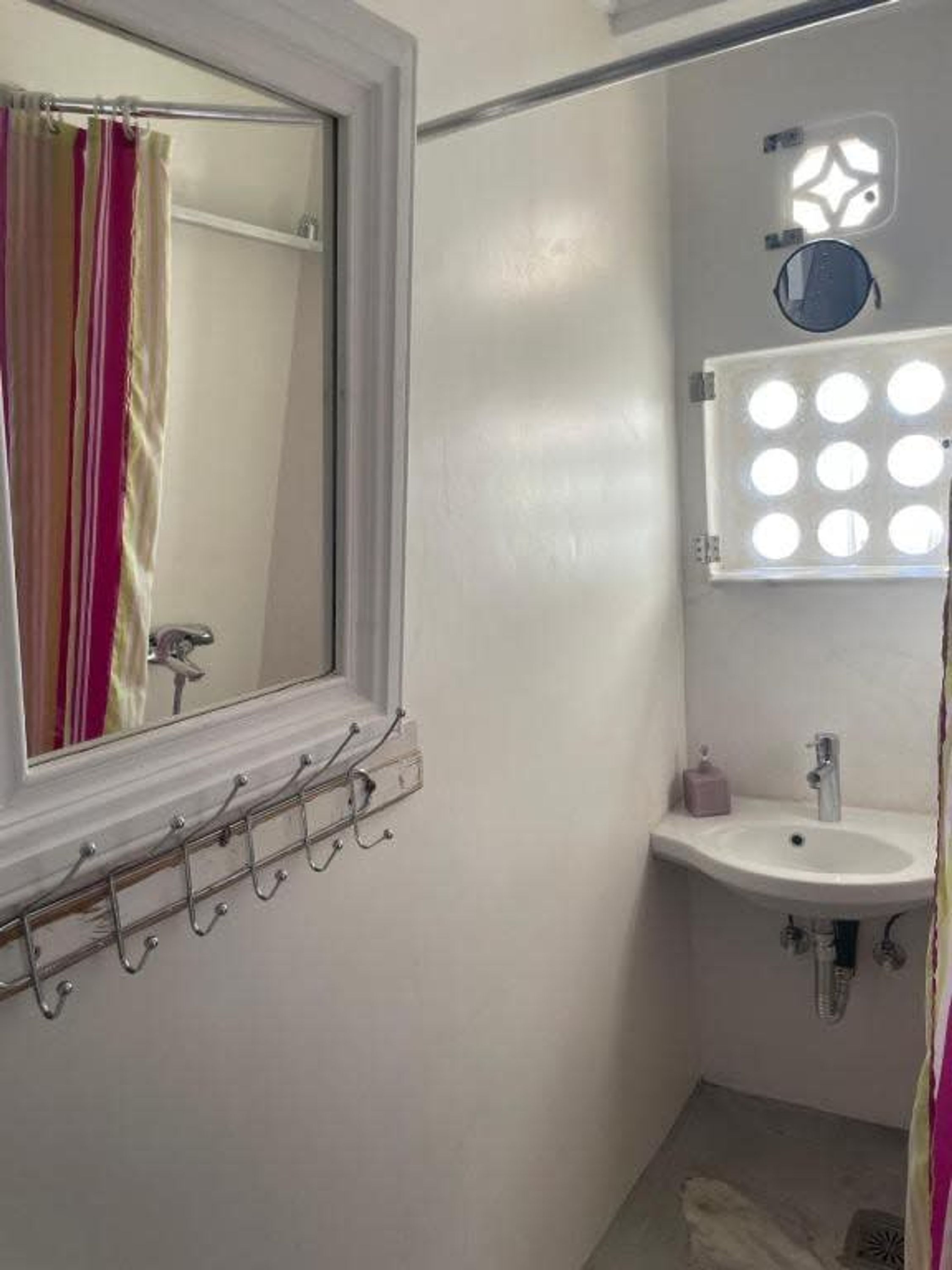 A bathroom with a window, a mirror, a sink, and a vanity with a light fixture above it.