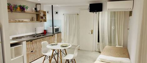 A compact hotel room with a kitchenette, a dining area with two chairs, a bed, and a TV mounted on the wall.