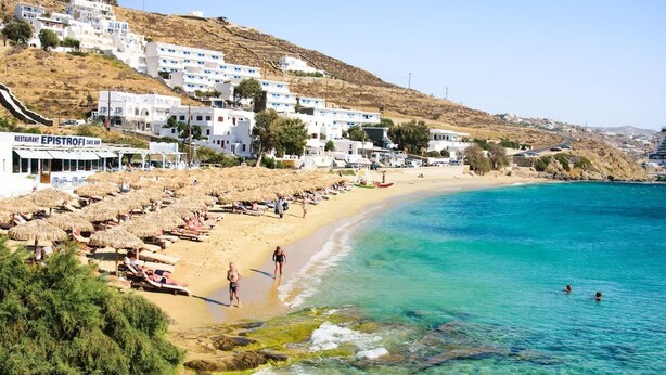 Une ville côtière aux bâtiments blancs, une plage parsemée de parasols et une eau d’un bleu limpide.