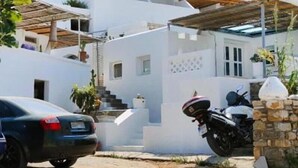 Un bâtiment moderne aux murs blancs, surmonté d’un toit en bois, avec une voiture et une moto garées devant.