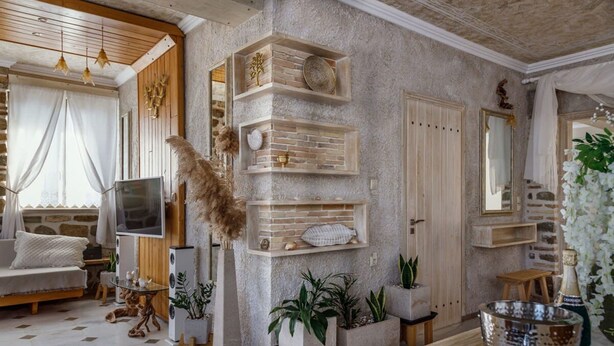 A living room with a stone wall, wooden shelves, a sofa, a TV, and a decorative plant. - Lithos Messolongi Paradise - A Luxurious Retreat (Mesolongi)
