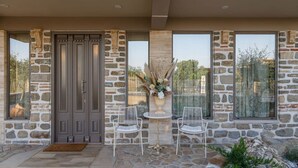 A stone facade with a double door, two white chairs, and a small table with a vase of flowers. - Lithos Messolongi Paradise - A Luxurious Retreat (Mesolongi)