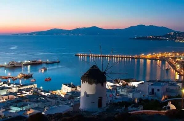 A coastal town at dusk with a windmill, boats, and a pier.