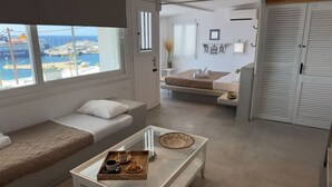 A modern hotel room with a large window overlooking a marina, a sofa, a bed, and a small dining area with a tray of breakfast. - Mykonos Noir Nest - Sea View Escape (Mykonos)