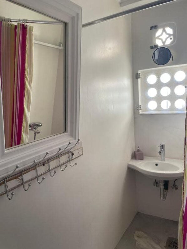 Une salle de bain avec une fenêtre, un miroir, un lavabo et un meuble-lavabo sur lequel est fixée une lampe.