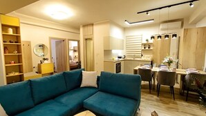 Ένα μοντέρνο σαλόνι με έναν τιρκουάζ καναπέ, ένα τραπεζάκι σαλονιού και μια τραπεζαρία με ένα ξύλινο τραπέζι και καρέκλες.
