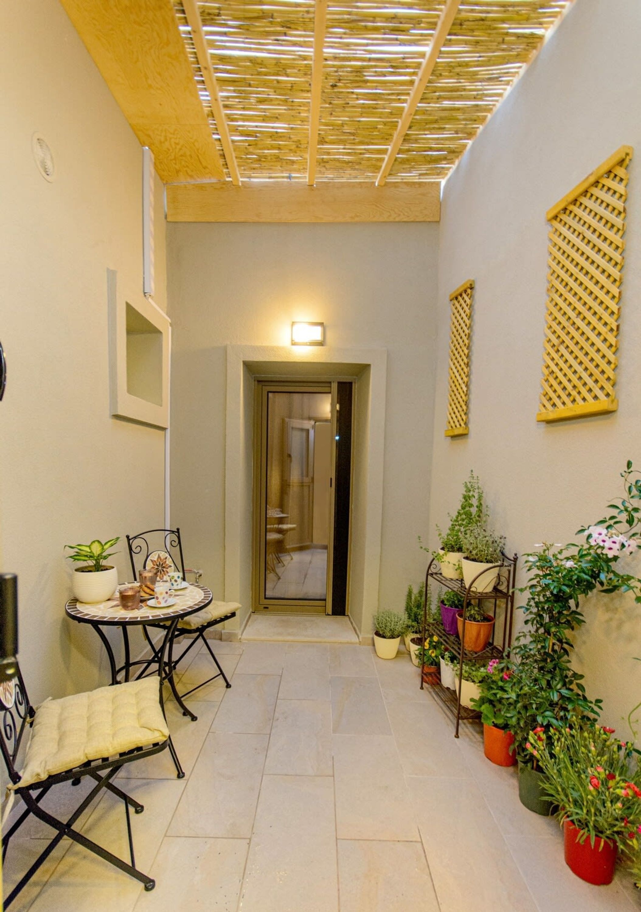 A narrow corridor with a tiled floor, a small table with chairs, and potted plants on one side.