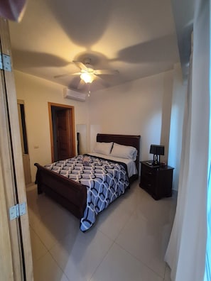 Een slaapkamer met een bed, nachtkastje, plafondventilator en een airconditioning.