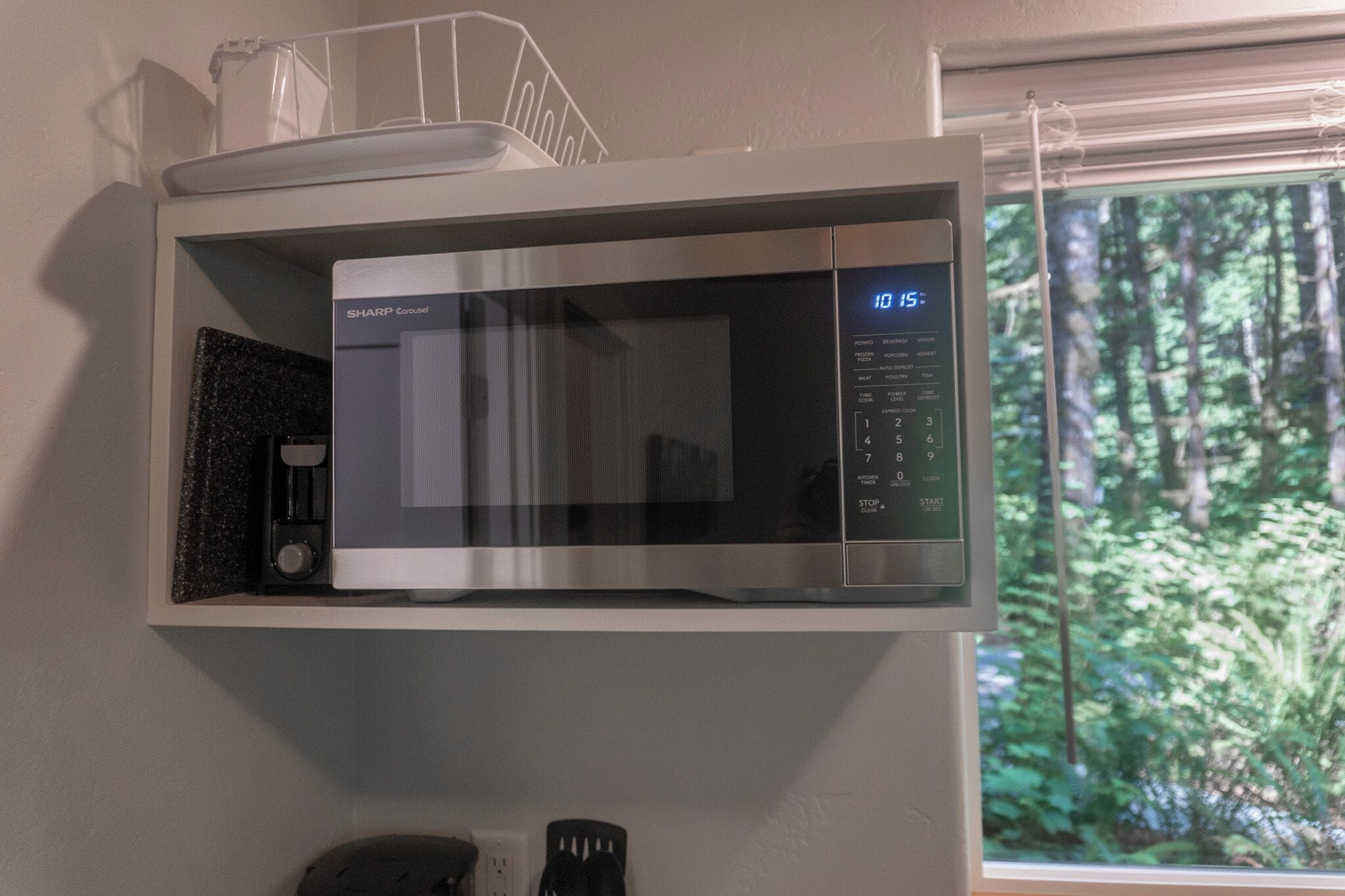 A microwave oven mounted on a white wall, with a digital display showing the time.