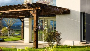 A modern building with a wooden pergola covered in purple flowers, a glass entrance, and a grassy area with yellow flowers in front. - Escape to a Charming Villa in Haut-Doubs. (Bians-les-Usiers)