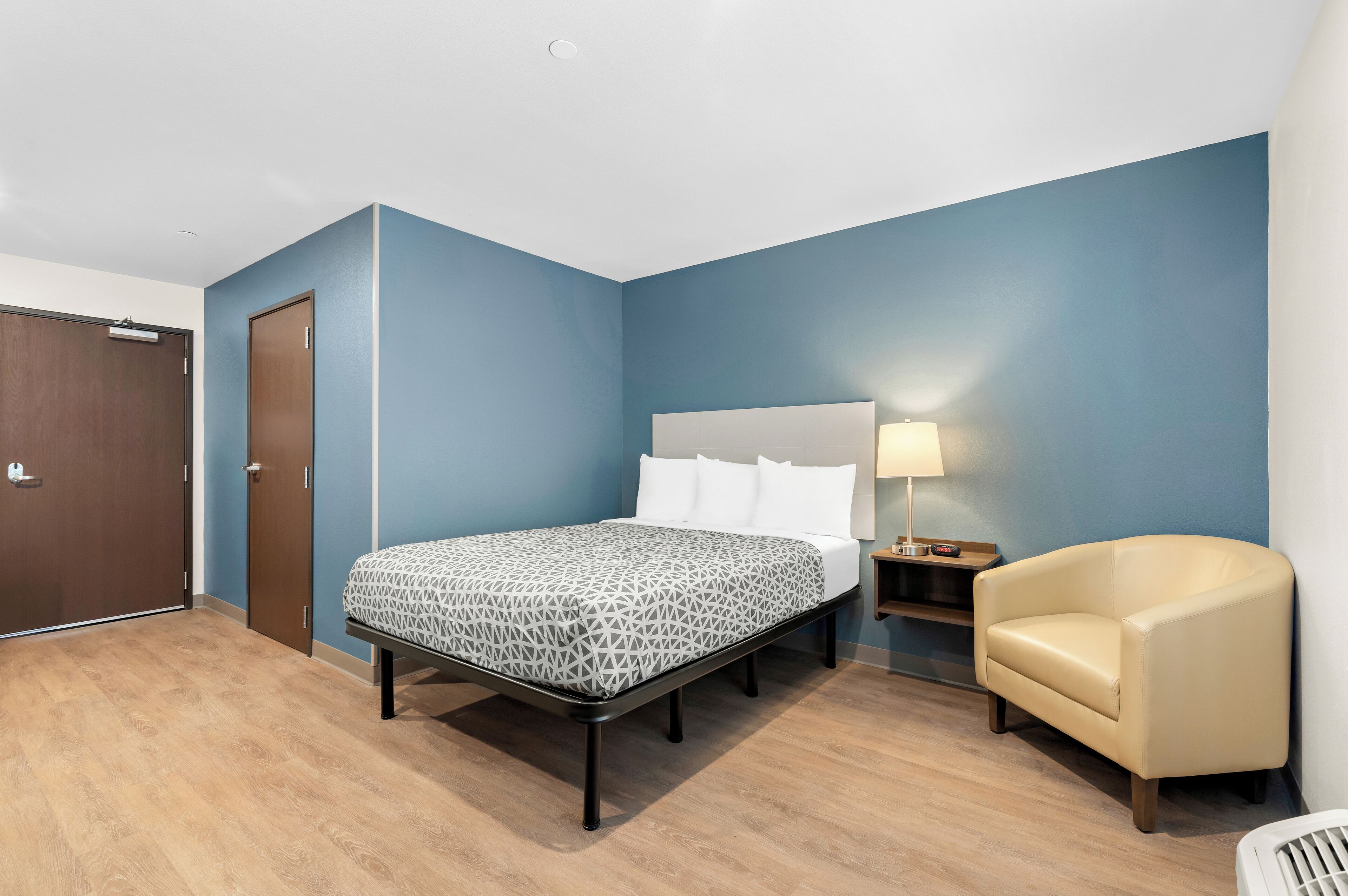 Une chambre d’hôtel avec un lit, une chaise, une table de chevet et une porte.