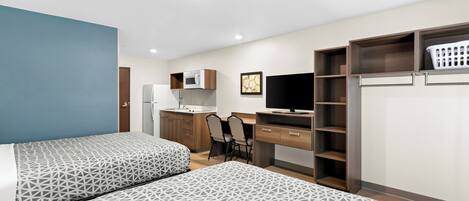 Une chambre d’hôtel avec deux lits, un bureau, une chaise, une télévision, un four à micro-ondes et un panier à linge.