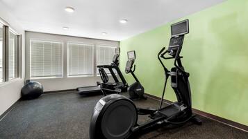 A gym with exercise equipment, a large window with blinds, and a green wall.